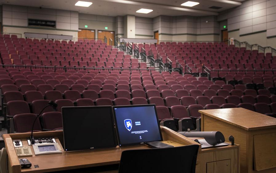 A computer screen is lit up at a podium overlooking an empty 的ater classroom.